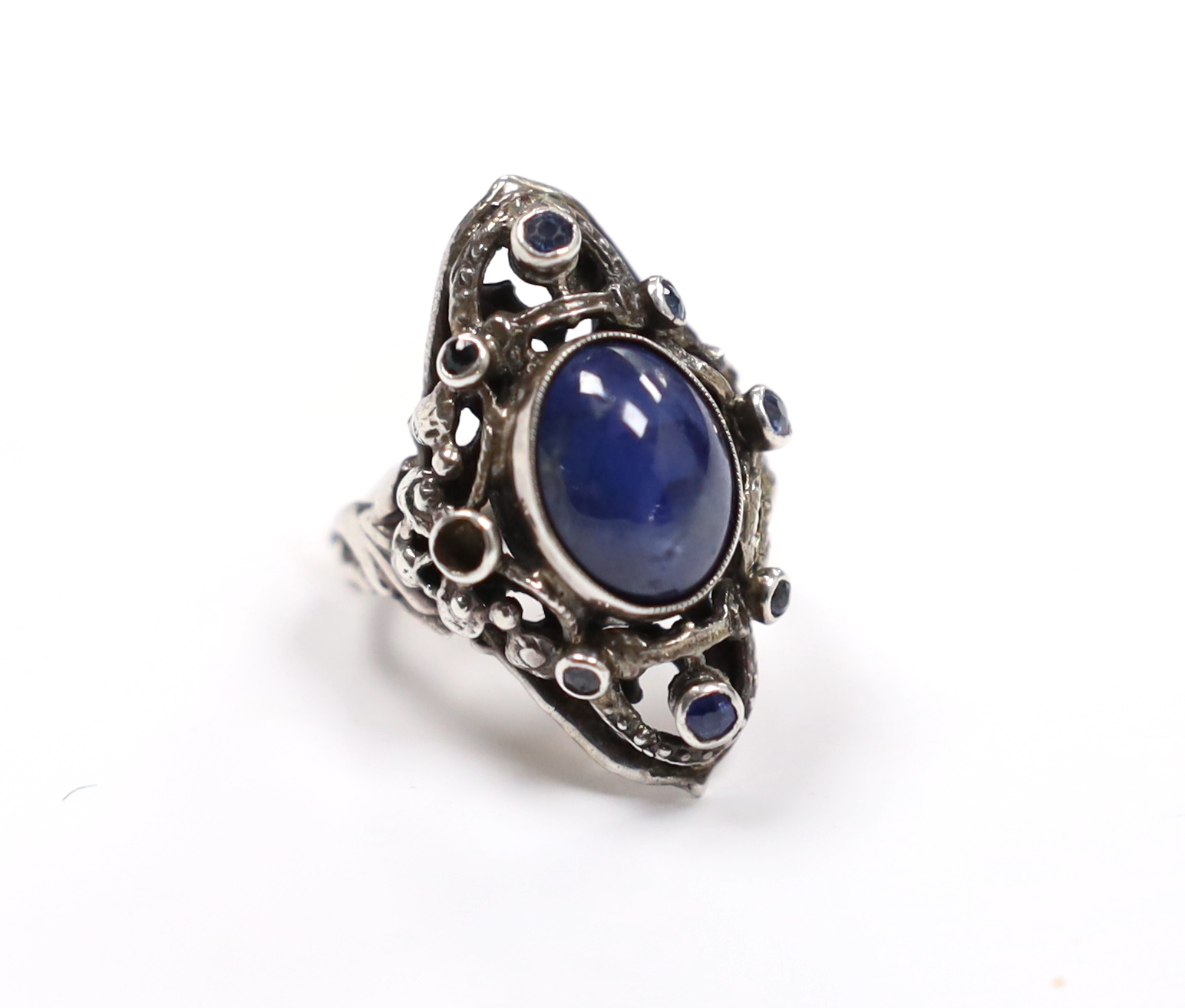 An Arts & Crafts pierced white metal and blue cabochon set dress ring, bordered with seven (ex 8) blue stones, size M.
